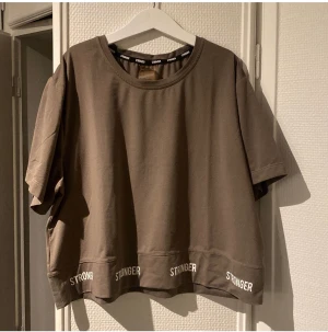 Stronger träningströja - Grå/grön träningströja från stronger. T-shirten är i ”vanligt träningströj-material. Den är även väldigt vid och ungefär navellång