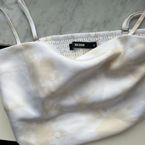 Fin topp från bikbok i silkesmaterial😍🤍 - Vacker vit topp med guldiga/beiga detaljer ifrån bikbok! Sitter jättebra och är knappt använd, Nyskick💖