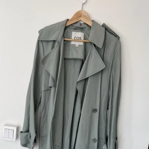 COS trenchcoat grön - Grön trench coat från COS i en ocersized modell (superfin men säljer då den inte kommer till användning). Nyskick då den endast är använd vid ett tillfälle🌼 