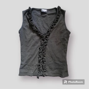 Svart topp med volanger - En cool vintage svart topp med volanger  Okej skick, finns små skavanker (volangen har lossnat i en söm längst ner) därav priset. 