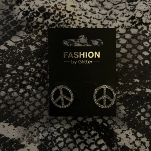 Örhängen  - Silvriga örhängen med peace märke från Glitter. Aldrig använda.