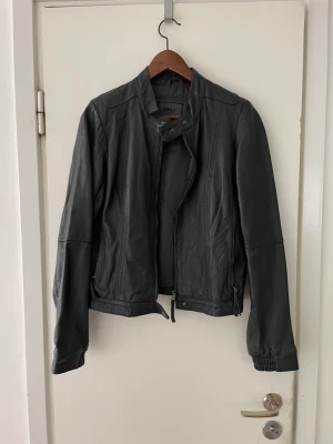 Jacka i skinimitation  - En mörkgrå jacka i skinimitation  I mycket fint skick. Kan skicka flera bilder. Samfraktar 