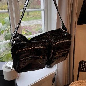 Noelle Väska  - En svart lackväska från Noelle, rymlig och bra storlek på axelväska, får plats mycket i den. Har en liten innerficka. 