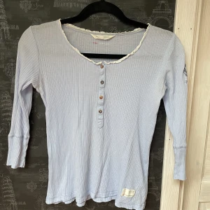 Oss Molly tröja - Oss Molly tröja  Ljusblå ribbad Knappar i fram, liten spets runt halsen Sparsamt använd Ros och rosett