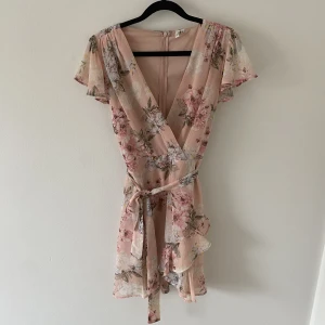 Blommig klänning - Blommig klänning i ljusrosa från Nelly. Volang på axlar och går att knyta i midjan. Storlek 36