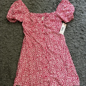 Helt ny klänning - Jättefin rödblommig oanvänd klänning från Nelly i storlek 34, säljer då den tyvärr inte passade mig.  Säljer för 80 kr, kan mötas upp i Kalmar eller skickas mot fraktkostnad.
