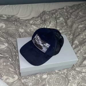 Blå fluffig keps - Mörkblå keps med en gammaldags racingbil på framsidan, en av piggarna där man justerar storleken på kepsen är av och jag tror en annan är lös. Priset går att pruta ner