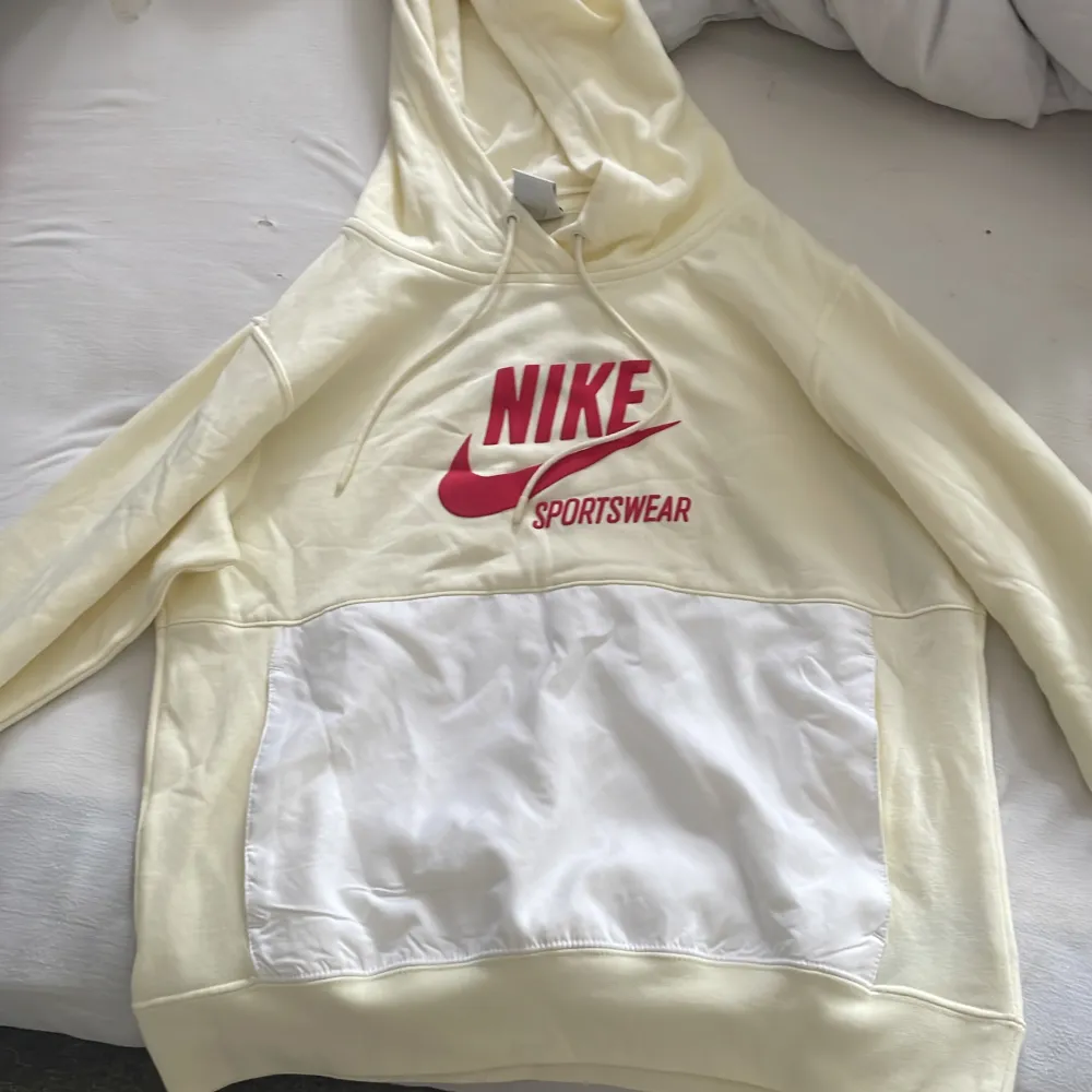 Vi säljer en Nike sportswear hoodie. Den är i storlek xs. Beige med röd text och vita fickor. Den har aldrig använts och lappen sitter kvar.VIKTIGT: vi kommer inte att betala för frakt. Hoodies.