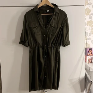 Knyt klänning  - En väldigt mörk grön knyt klänning med två fickor och ärmar som är invikta permanent. Den är gammal men oanvänd och är i väldigt bra skick. 