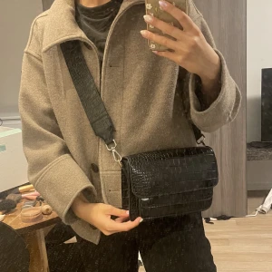 Axelremsväska - Säljer min svart axelremsväska i sådant där coolt snakeskin mönster. Själva väskan är från NA-KD och axelremsbandet är från Carin Wester. Säljer då den inte kommer till användning