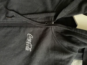 coca Cola Hoodie  - Hoodie använd fåtal gånger. Svart med tryck fram och bak. Dragkedja 