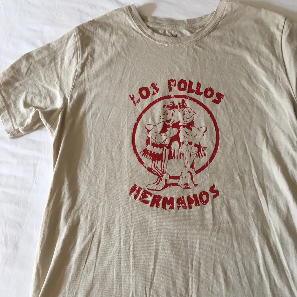 Unik beige T-shirt med handgjort ”Los Pollos Hermanos” tryck på!! OBS! Finns en liten fläck på, fråga för tydligare bild, (Trycket håller i tvätten, tvätta ut och in). T-shirts.