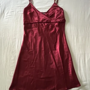 Vinröd vintage satinklänning - Ursnygg vinröd vintage satinklänning med justerbara axelband och knytdetalj under bysten. Begagnat skick, men inga fläckar eller hål! Storlek 42🫶💕