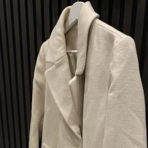 Beige Kappa - Säljer denna fina oanvända kappa. Den är rätt så lång och har ett rätt så tjockt/varmt material. Perfekt nu inför hösten. Är san till storlek så varken för stor eller för liten. 🍂