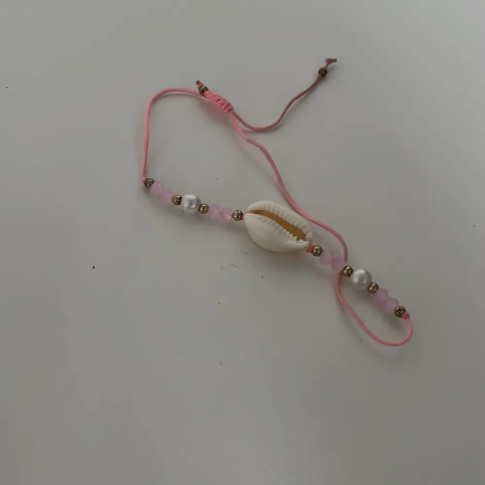 Ett armband med rosa tråd, lite pärlor och en snecka. Köpt för ungefär 1€ utomlans. Aldrig använt. Accessoarer.