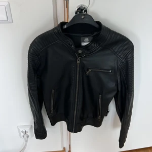 Svart jacka i konstläder - Svart jacka i konstläder säljes i befintligt skick.  Passar XS.