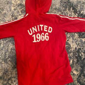 En röd zip up hoodie med vita detaljer, lite kortare model i armarna, text på ryggen