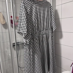 Svartvit houndstooth klänning - Svartvit houndstooth klänning  Satin, polo neck   Fint skick, använt bara 2 gånger  Storlek runt 52, elastisk midja 