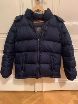 Polo Ralph Lauren Dunjacka - En snygg blå Polo Ralph Lauren dunjacka till vintern. Jackan är i bra skick förutom att Polo-märket är utnött. Säljer då jag har vuxit ur jackan. Storleken är L (14-16) vilket blir XS-S i vuxenstorlekar.