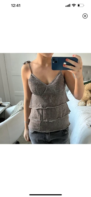 Silvrig volangtopp - Säljer denna underbara gråa/silvriga volangtopp 😍knappt använd, väldigt bra skick och banden är justerbara. (bild 1 lånad). Möts upp på Östermalm eller fraktar 