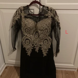 Festklänning, oanvänd! - Ursnygg festklänning som säljs på grund av för liten storlek. Helt ny, då den har aldrig använts! Är svart med guld detaljer. Är ganska lång, kontakta för mer bilder!