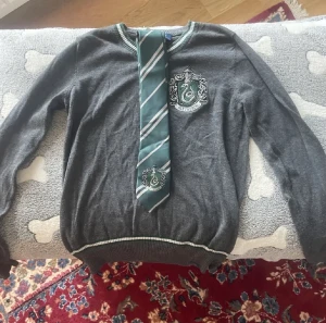 Slytherin kit - Säljer detta slytherin kit som innehåller 1 slytherin stickad tröja, några slytherin tatueringar, 1 slytherin kappa, 1 slytherin slips och 1 slytherin kjol. Allt är i nyskick. Passar barn runt 8-10 år. Kontakta mig vid intresse eller frågor. :)