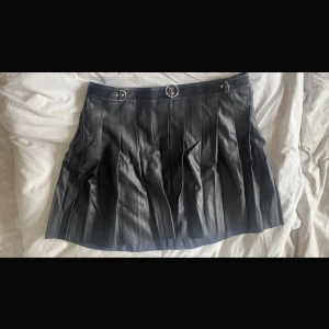 Plisserad kjol i skinnimitation med silverdetaljer - En kjol i läderimitation med silverdetaljer och hög midja ifrån märket Current Mood inhandlad på Dollskill i storlek 2XL (xxl). Stängs med dragkedja på baksidan. Aldrig använd.   Midja 49cm Längd på kjol 54cm