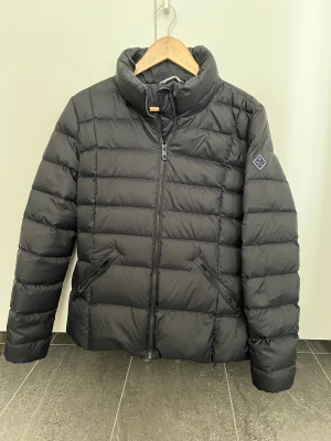 Gant classic dunjacka dam - Tjock dunjacka svart storlek L men mer som en M. Använd endast ett fåtal gånger. Tjock avtagbar kapuschong med tryckknappar. Dragkedja på fickorna. 