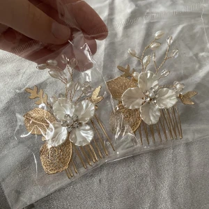 Hårspänne - Ett jättevackert guldigt hårspänne med vita blommor samt kristaller på. Då jag har 2 stycken kan de antingen köpas tillsammans eller separat. Pris; 30kr styck. Skriv för mer info och bilder.