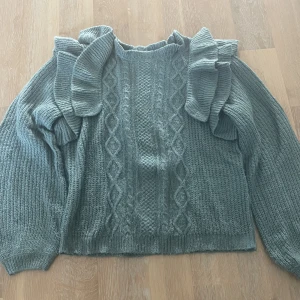 Grön blå stickad tröja - Grön blå fint stickad tröja med volanger på axlarna och stickat mönster på magen. Säljer då den sällan kommer till användning, alltså är den i bra skick. Pris kan diskuteras. Köparen betalar frakt.