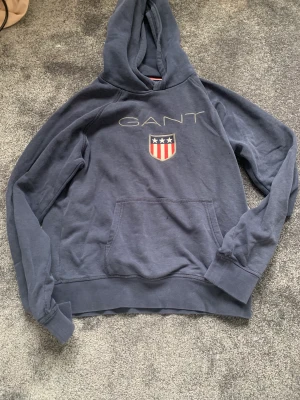 Marinblå gant hoodie - En marinblå gant hoodie med stort tryck där fram där det står GANT. Köpt för 800kr. Har även en svart likadan.