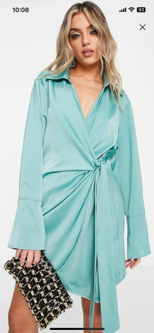 Turkos omlottklänning i satin - Helt ny klänning, aldrig använd. Turkos omlottklänning i satin. Perfekt att klä upp eller ner beroende på tillfälle.