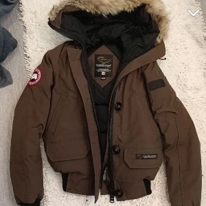 Canada Goose  - En väldigt fin Canada Goose vinterjacka i fin bryn färg. Jättebra skick 10/10. Använd fåtal gånger. Här av er om ni vill ha mer information.  Storlek xxs-xs
