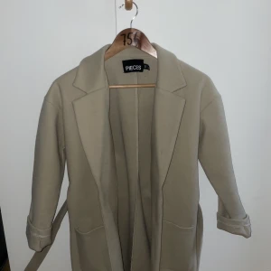 Beige kappa  - Andvänd fåtal gånger. En lite tunnare kappa till våren. Passar dig som har Xs i vanliga fall. Kontakta vid frågor m.m..
