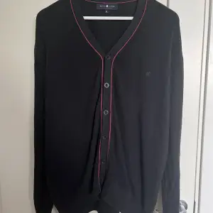En mörkblå kofta/tröja med röda detaljer köpt secondhand. Den är i bra skick och har stretchig material!! Storlek XL