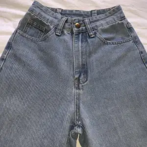 Högmidjade jeans som är insydda i midjan. Har slitningar längst ner på benen, se bild. Midjemått ca 62cm. Innerbenslängd ca 76cm. Vikt ca 350g. 