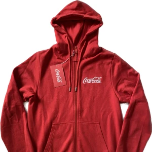Zip hoodie Coca Cola - Jag säljer nu syrrans inprincip oanvända hoodie från Coca Cola då den enbart hänger i garderoben och tar plats. Den är som ny och har inga tecken på användning. Köptes från en Coca Cola shop för 600kr. Priset är inte hugget i sten Frakt betalar du själv!
