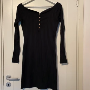 Mini klänning  - En kort figurnära klänning med hjärtformad u-ringning och knappar fram. Ribbad.