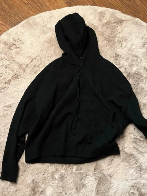 Svart hoodie med huva och dragsko - En stilren svart hoodie med huva och dragsko. Hoodien har långa ärmar och en avslappnad passform. Tillverkad i mjukt material som känns skönt mot huden. Perfekt för dig som gillar en enkel och clean look.