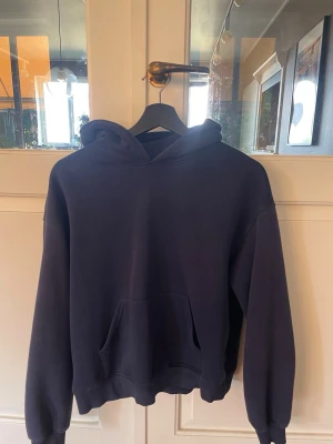 Mörkblå hoodie från Gina Tricot - En stilren mörkblå hoodie från Gina Tricot, kollektionen elevated basics. Hoodien har en klassisk huva, magficka och ribbade muddar vid ärmar och nederkant. Perfekt för en chill och avslappnad look.