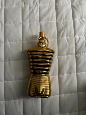 Jean Paul Gaultier  - Unik parfymflaska i metallisk guldfärg, formad som en manlig torso med horisontella svarta ränder. Flaskan har en elegant och modern design som sticker ut i badrumshyllan. Perfekt för dig som gillar exklusiva och iögonfallande detaljer.