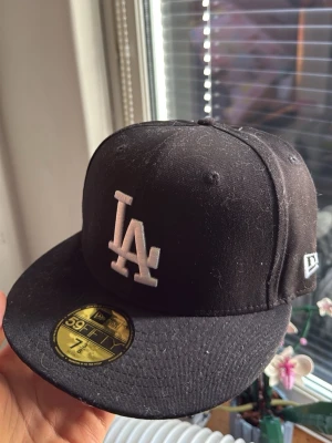 Svart LA New Era 59FIFTY keps - Säljer en svart New Era keps med LA-logga broderad i vitt framtill. Klassisk flat peak och strukturerad passform. Kepsen är helt oanvänd då den inte passade mig och den har alla lappar kvar