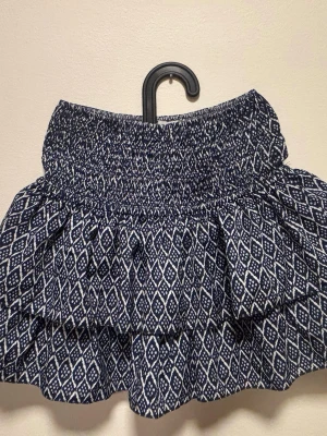 Mönstrad kortkjol från Meet x Tiger - Supersöt kortkjol från Meet x Tiger i blått och vitt med elastisk midja och volanger. Kjolen har inbygda shorts. 