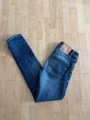 Jack&jones slim fit jeans - Snygga blå slim fit jeans med tydliga slitningar och tvättade detaljer. Klassisk femficksmodell med normal midja och smala ben. Jeansen har en läderpatch bak i midjan och är tillverkade i denim, perfekt för en trendig vardagslook.