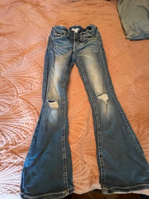 Blå bootcut jeans med slitningar - Säljer ett par blå bootcut jeans med slitningar på knäna och snyggt broderade bakfickor. Jeansen har en ljus tvätt och är tillverkade i klassisk denim.🥰❣️