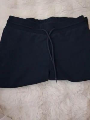 Mörkblå mjukisbyxor med dragsko - Säljer ett par mörkblå mjukisbyxor med raka ben och dragsko i midjan. Byxorna har en enkel och clean look, perfekta för chill dagar hemma eller när du vill vara bekväm. Materialet känns mjukt och skönt mot huden.