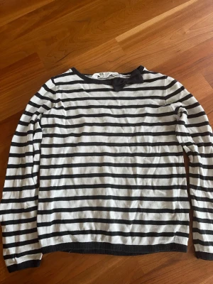Randig stickad tröja med rosett - Snygg stickad tröja från H&M med svartvita horisontella ränder och en söt svart rosett vid halsringningen. Tröjan har långa ärmar och ribbade muddar. Perfekt för dig som gillar klassisk stil med en twist. Ska strykas vid köp!🖤🤍