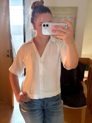 Vit kortärmad skjorta med ficka - Säljer en vit skjorta i luftig bomull med korta ärmar och en bröstficka. Skjortan har knappar framtill, avslappnad passform och krage. Perfekt till jeans eller kjol för en enkel och fräsch look.🫶🏼🫶🏼