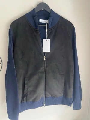 Gran sasso Cardigan ny - Snygg gran sasso Cardigan i svart mockaimitation framtill och marinblå stickade ärmar och muddar. Jackan har dragkedja, två fickor fram och ribbad krage. Perfekt för dig som vill ha en stilren och modern look. Helt ny