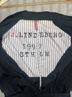 Kappa J.Lindeberg - Snygg svart Kappa från J.Lindeberg med klassisk design. Perfekt för blåsiga dagar och enkel att matcha till olika outfits.